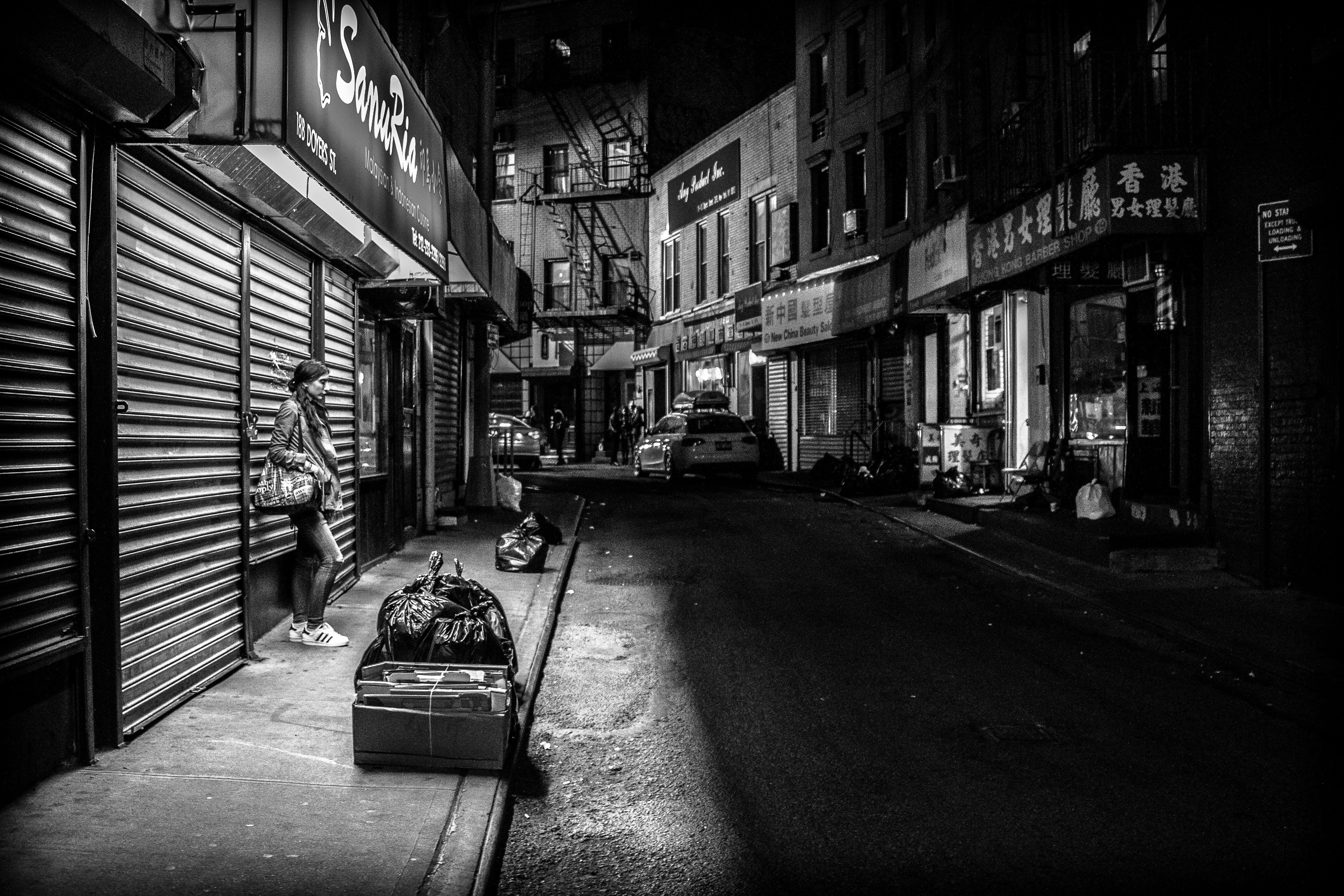 grayscale photography of woman standing infront of store shutter door at night